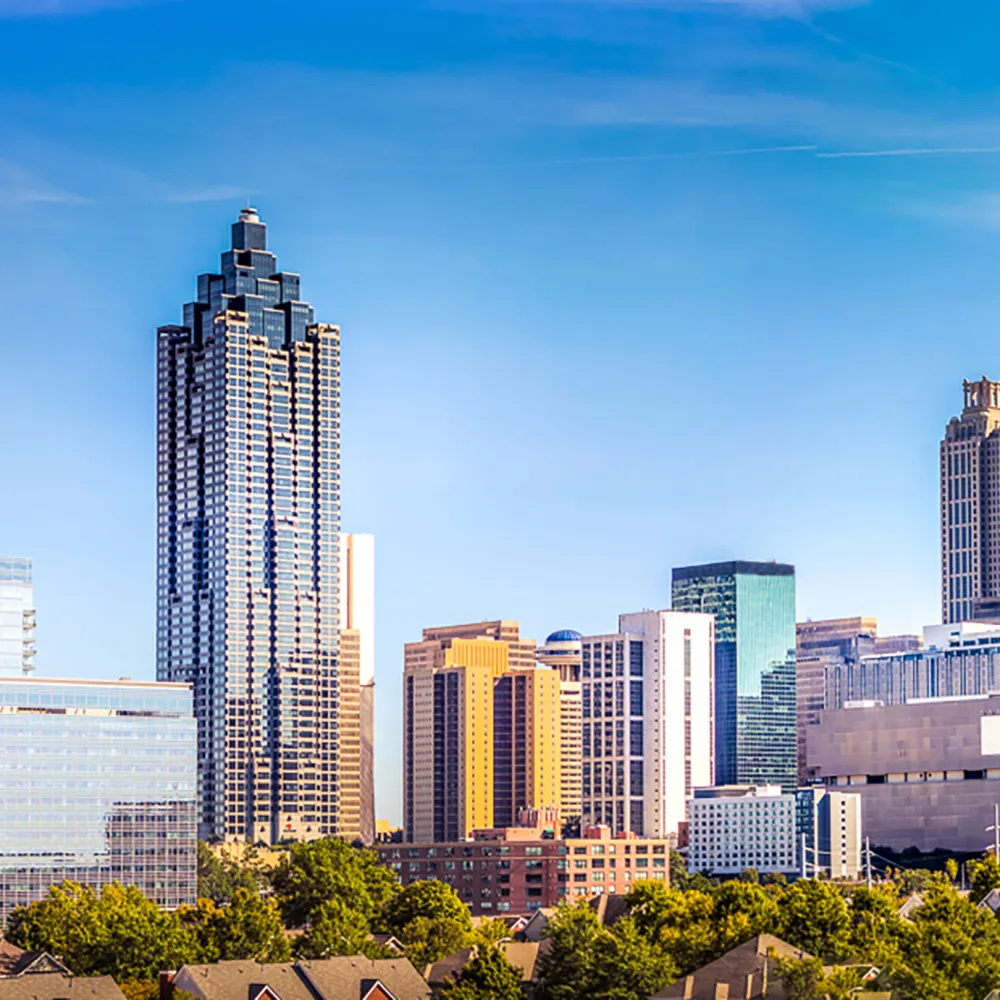 Bright daylight view of Atlanta skyline with tall buildings and lush green trees in foreground.
