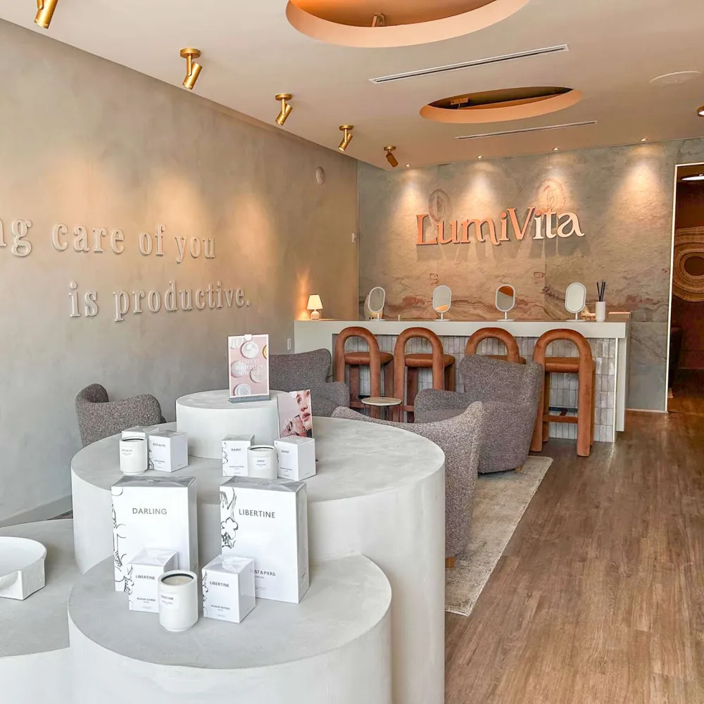 Modern spa interior with gray chairs, wooden bar stools, skincare products on round displays, and motivational wall text.