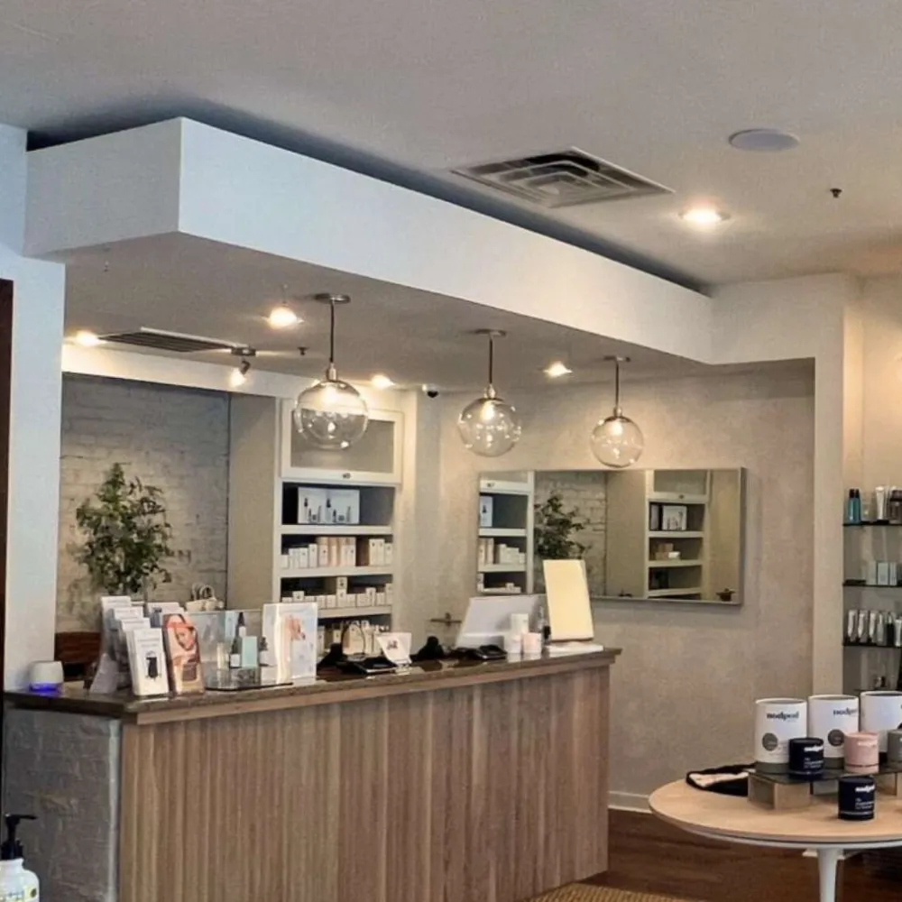 Modern spa reception with wooden counter, pendant lights, product displays, and neutral-toned decor.