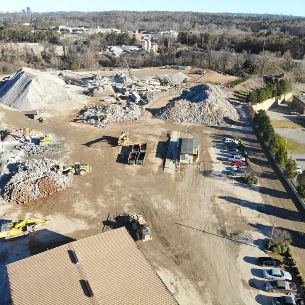 Aerial view of an industrial site with piles of gravel, heavy machinery, and parked vehicles near railway tracks.