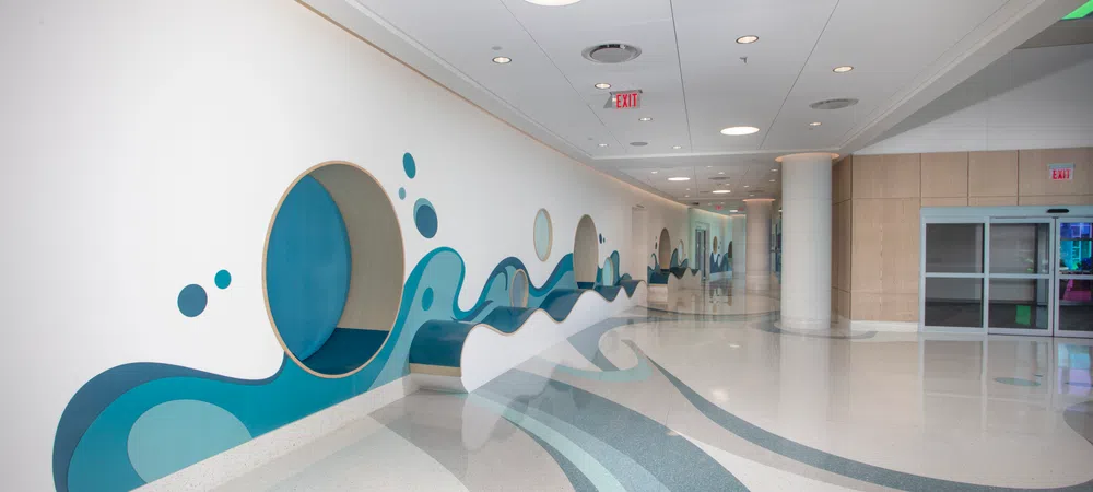 Modern hallway featuring blue wave mural with circular cutouts and smooth curved floor patterns in bright space.