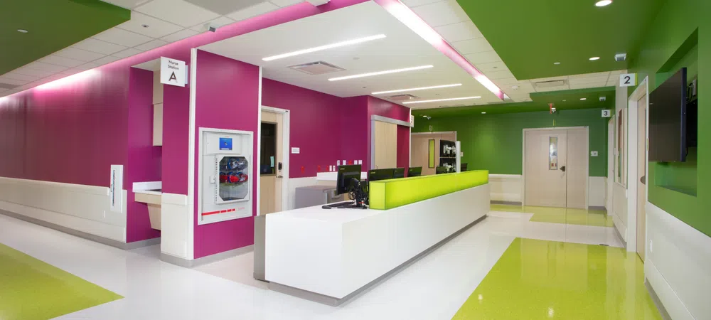 Modern hospital reception area with vibrant green and magenta walls and white floors under bright lighting