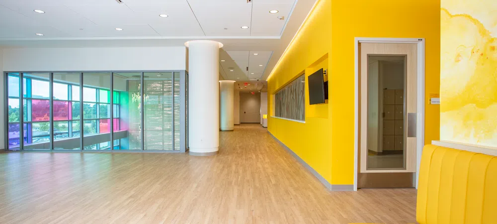Bright modern hallway with yellow walls, wood flooring, and colorful glass panels on windows in an office building.