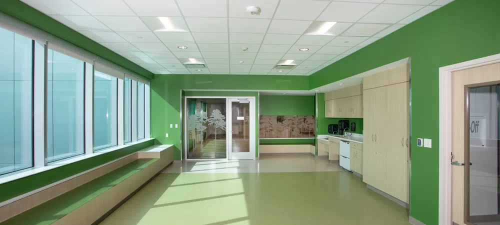 Bright green and beige room with large windows, storage cabinets, and sliding glass doors in a modern building.