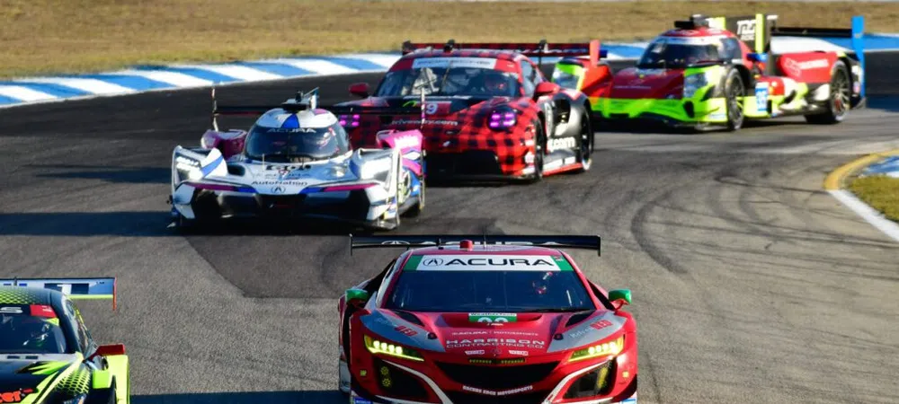 Multiple high-performance race cars competing on a curved race track during a sunny day event.