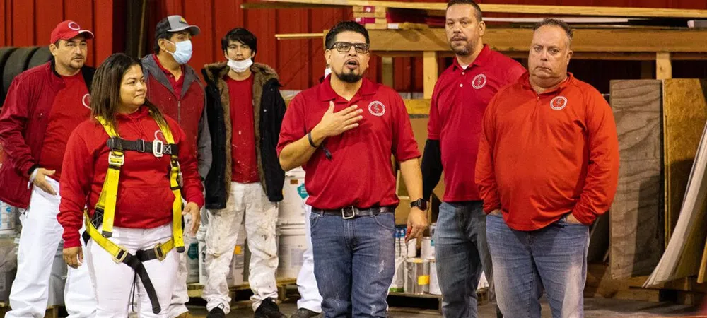 Group of workers in red shirts and safety gear standing indoors in a warehouse or workshop setting