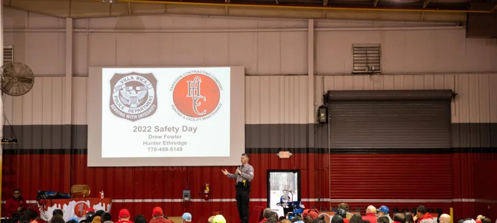 Audience listens to a presenter at 2022 Safety Day event with police and contracting company logos on screen.