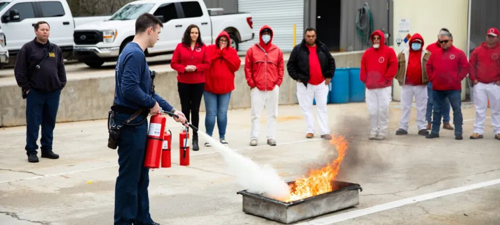 Fire safety training with instructor using fire extinguisher to put out controlled fire while group watches