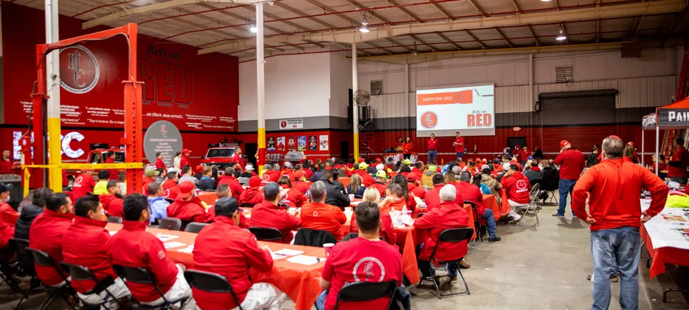 Large group of people in red shirts attending a safety training event in a spacious industrial warehouse.