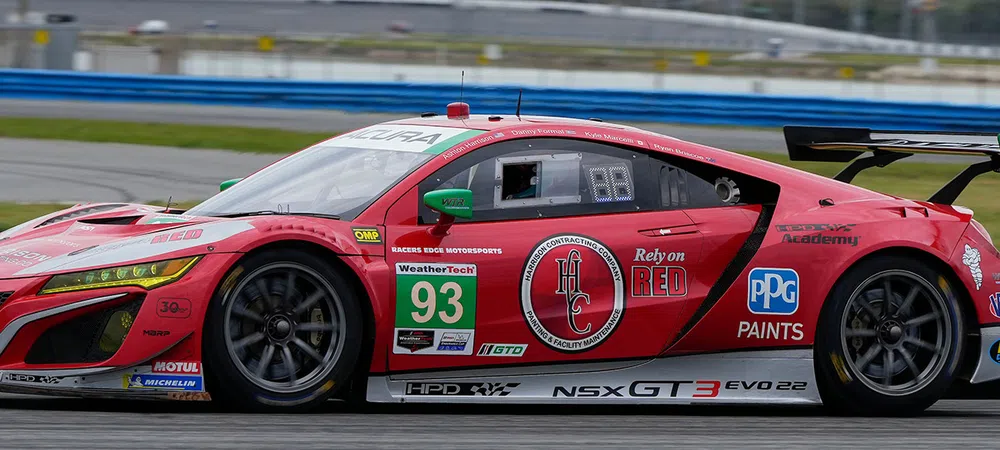 Red Acura NSX GT3 race car number 93 speeding on racetrack with sponsor logos and aerodynamic rear wing