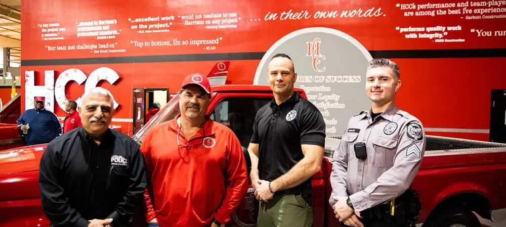 Four men standing in front of a red maintenance truck with HCC signage and testimonials on the wall behind them