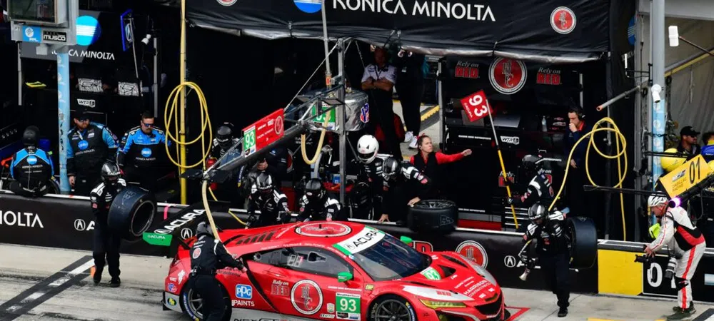 Race car number 93 in red at Konica Minolta pit stop during a motorsport event with crew working on tires.