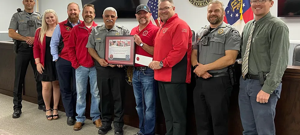 Group of police officers and civilians in a meeting room holding a framed certificate, smiling for the photo.