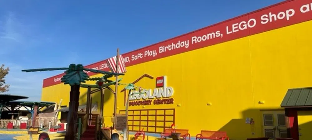 Bright yellow LEGOLAND Discovery Center building with colorful playground and clear blue sky overhead.