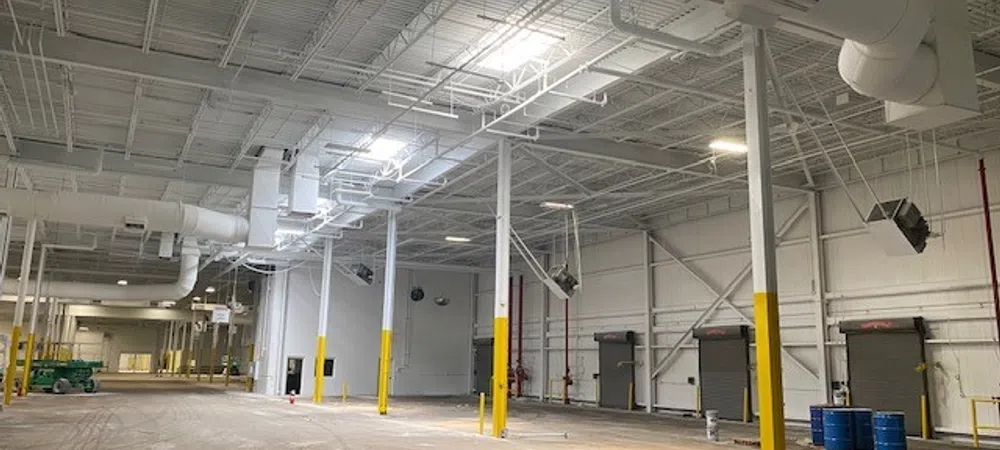 Spacious empty warehouse interior with high ceilings, yellow safety poles, and industrial lighting fixtures.