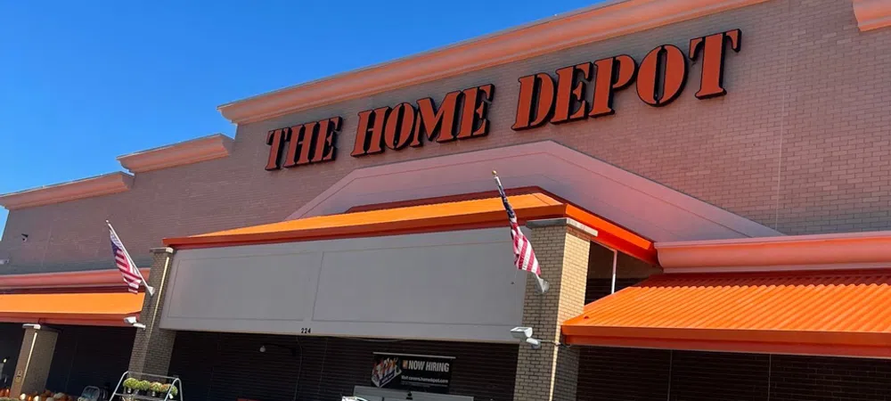 The Home Depot store exterior with orange awnings, American flags, and grills displayed outside on a sunny day.