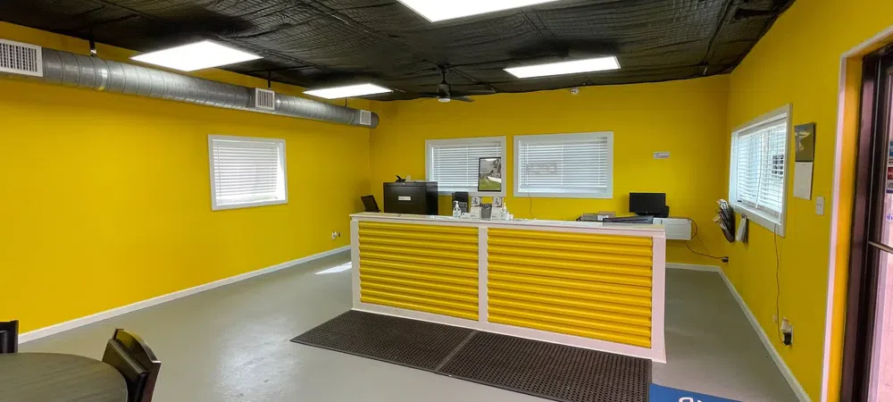 Bright yellow-walled storage facility office with white desk, black ceiling, and gray floor mats.