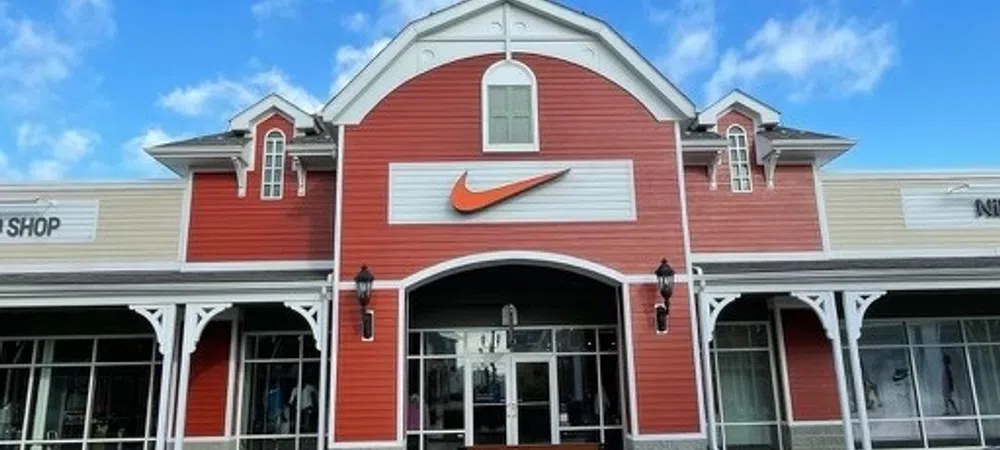 Exterior of a red and beige Nike store with a large orange swoosh logo under a blue sky