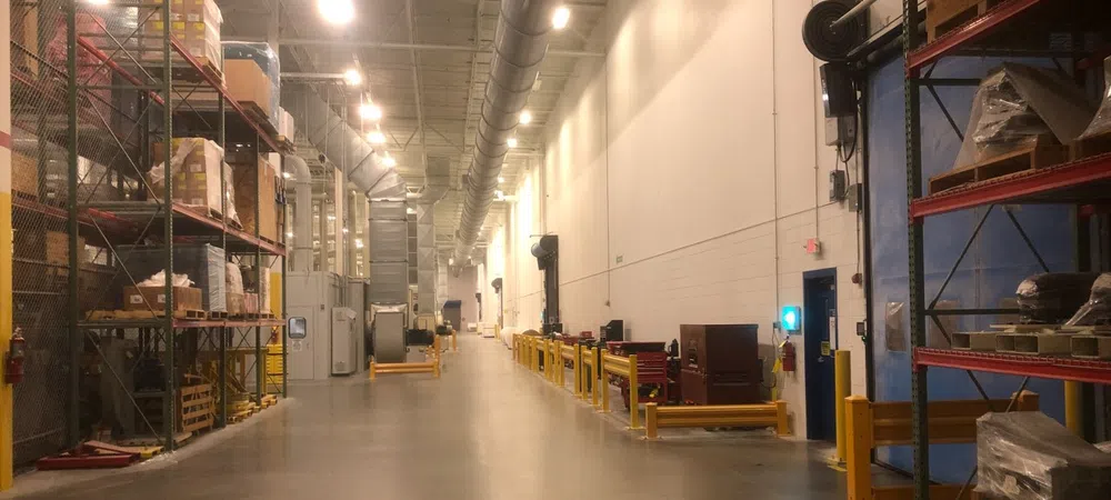 Spacious industrial warehouse aisle with shelves stocked with boxes and equipment under bright overhead lighting