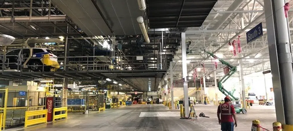 Large industrial warehouse with assembly lines, overhead conveyor systems, and a worker walking inside.