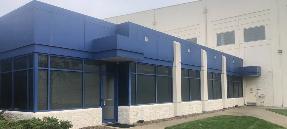 Modern commercial building with blue and white facade surrounded by green lawn and sidewalk.