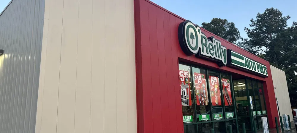 Exterior view of O'Reilly Auto Parts store with red and white facade and promotional posters on windows.