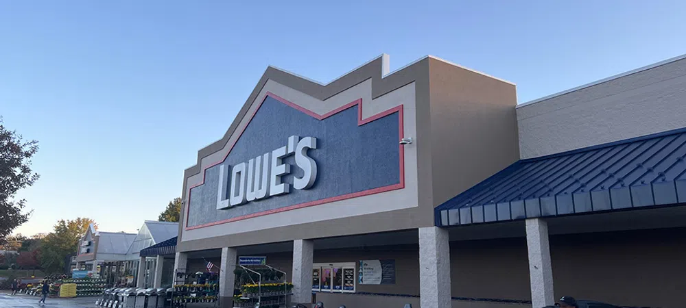 Exterior of Lowe's home improvement store with riding lawn mowers displayed outside on a clear day.