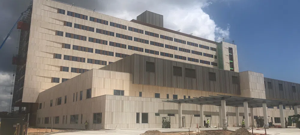 Modern multi-story hospital building under construction with clear sky and surrounding paved areas