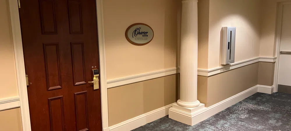 Hotel hallway with a wooden door labeled Charter Room, beige walls, white column, and patterned carpet.