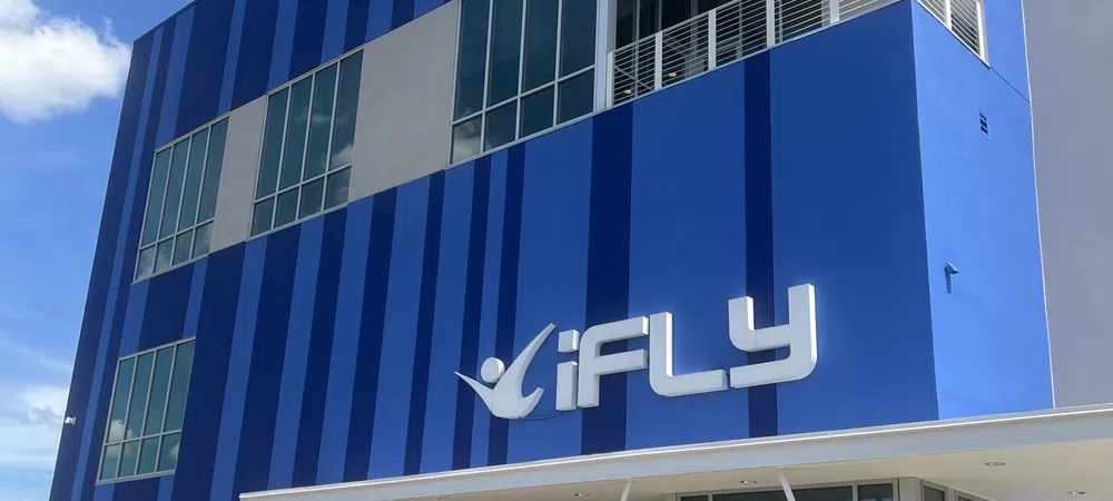 Modern blue iFLY building with large windows and a balcony, under a clear sky with scattered clouds.