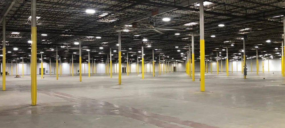 Large empty warehouse interior with yellow support columns and high ceiling lights evenly spaced.