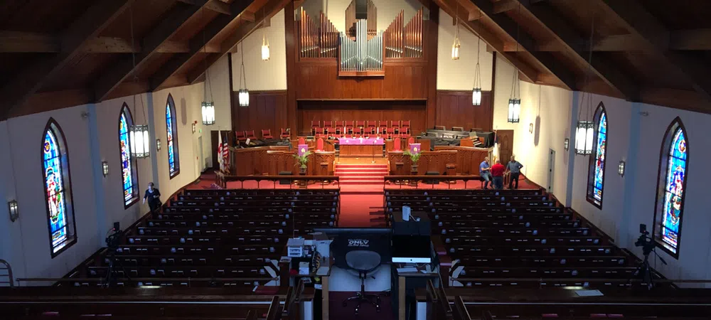 Interior view of a church with wooden pews, stained glass windows, an organ, and a high vaulted ceiling.