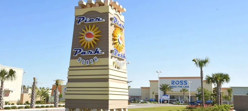 Pier Park North sign with sun logo in landscaped area near shopping center with Ross store in background