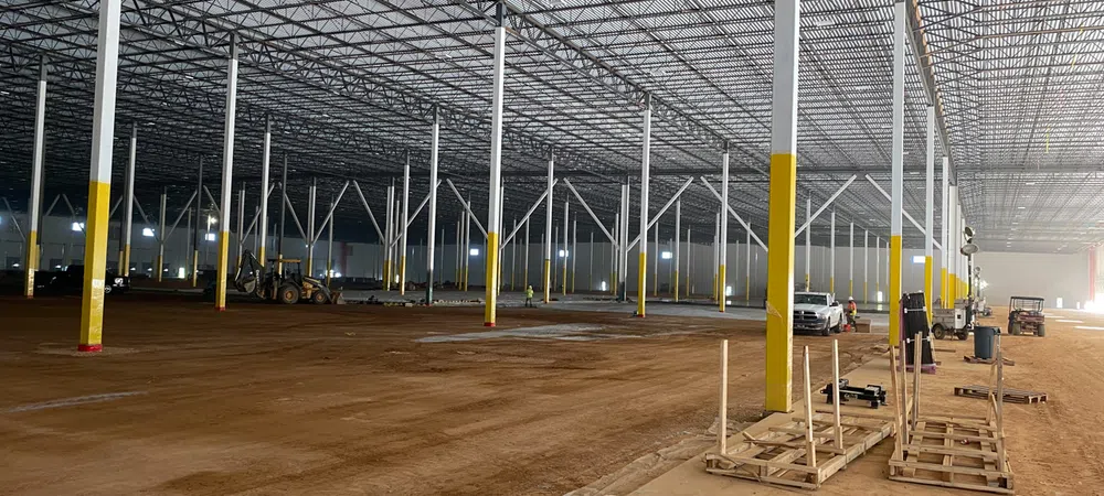 Large industrial warehouse under construction with steel columns and dirt floor extending into the distance