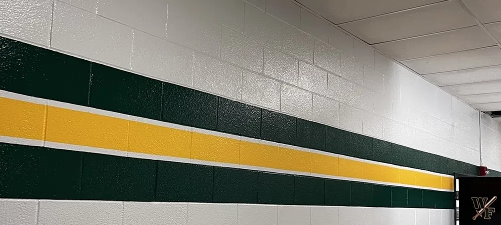White cinder block wall with green and yellow stripes leading to a door with WF logo under ceiling lights.