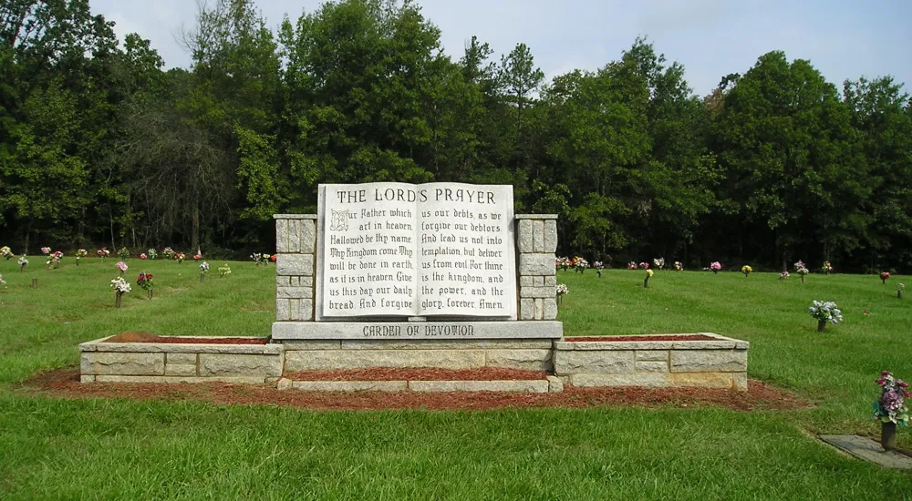 a large stone sign in a grassy field with trees in the background