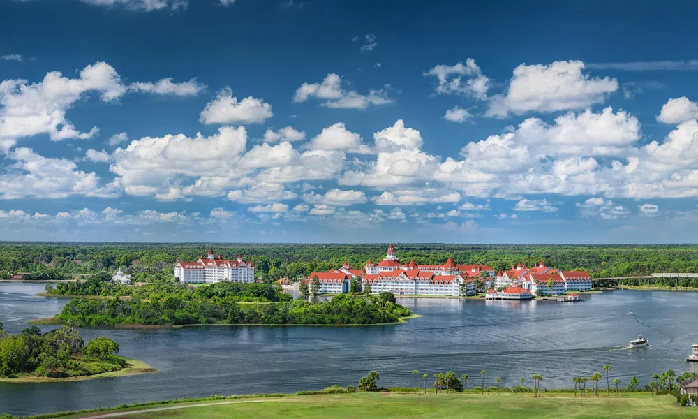 Panoramic view of a resort with red roofs surrounded by water, islands, and lush greenery under a blue sky with clouds