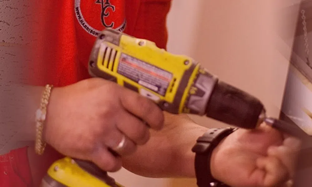 Worker in red shirt using a yellow cordless drill for a home improvement task indoors.