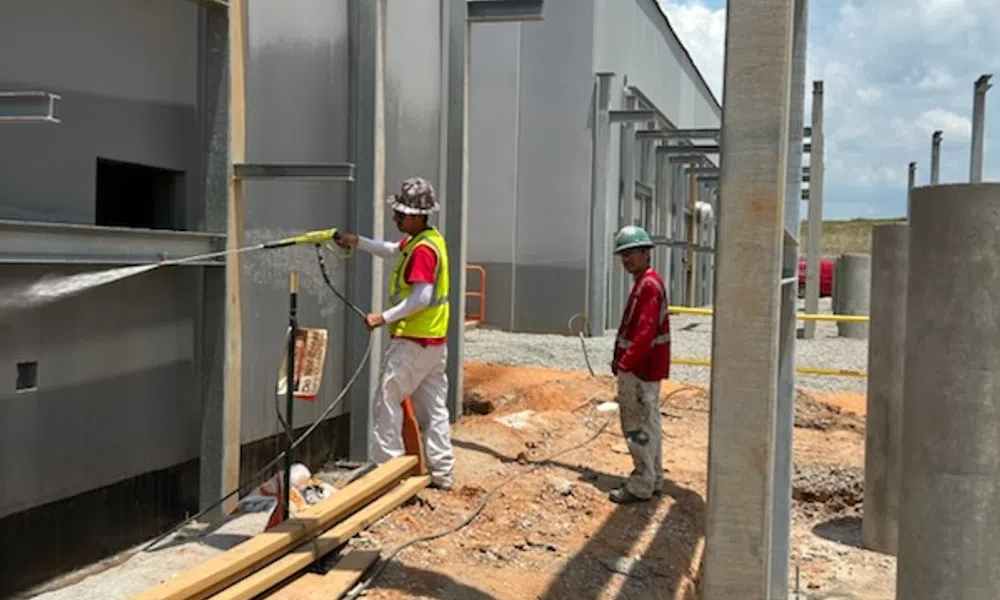 Two construction workers cleaning a building facade with a pressure washer on a sunny day at a construction site.