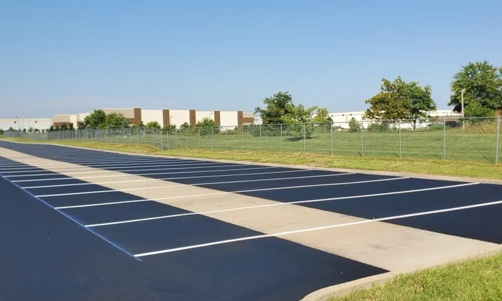 Empty outdoor shuffleboard court with clearly marked lanes, surrounded by grass and fencing under blue sky.