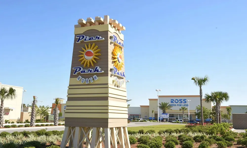 Pier Park North sign with sun logo in landscaped area near shopping center with Ross store in background