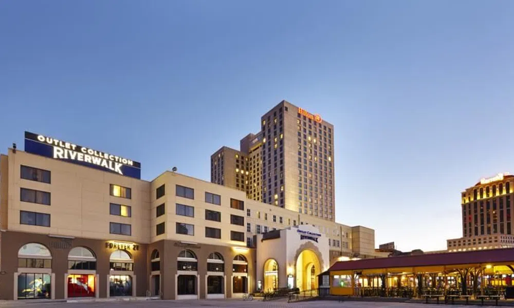 Outlet Collection Riverwalk shopping center and Hilton hotel at dusk with clear sky and illuminated signs.