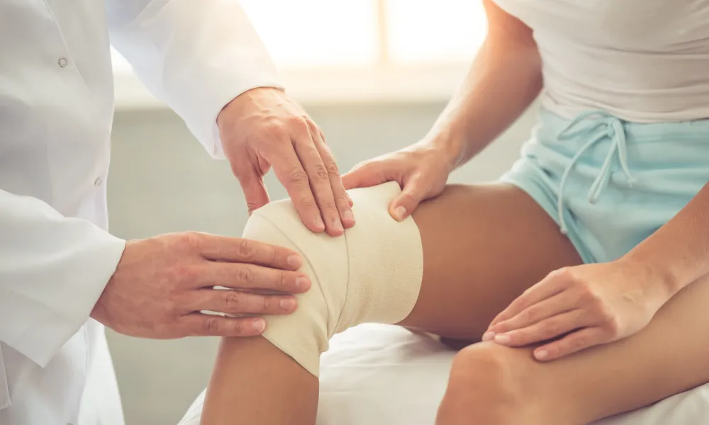 male doctor examining female patient's bandaged knee