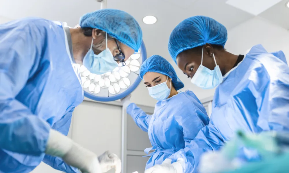 Medical professionals performing surgery in a sterile operating room environment with surgical lights.