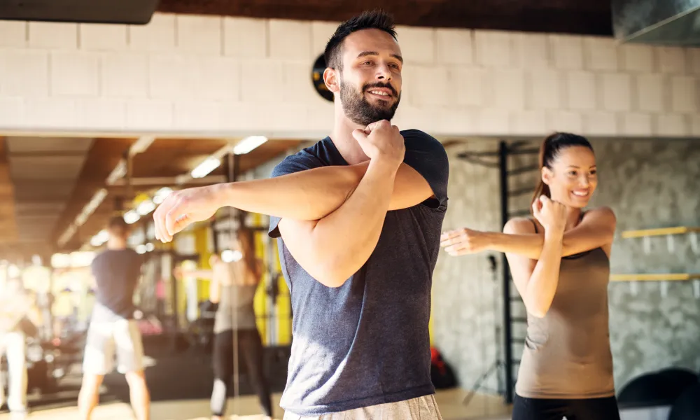 Man and woman stretching arms before workout in bright gym with mirrors and equipment