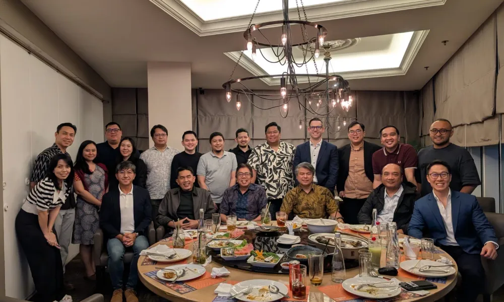 Group of diverse professionals posing around a dining table with food and drinks in a well-lit private room.
