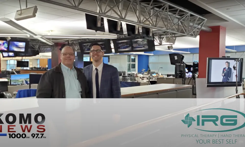 Two men smiling in a KOMO News newsroom with IRG Physical Therapy logo overlay.