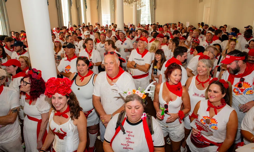 Large crowd dressed in white with red accessories gathers indoors celebrating a festive event.