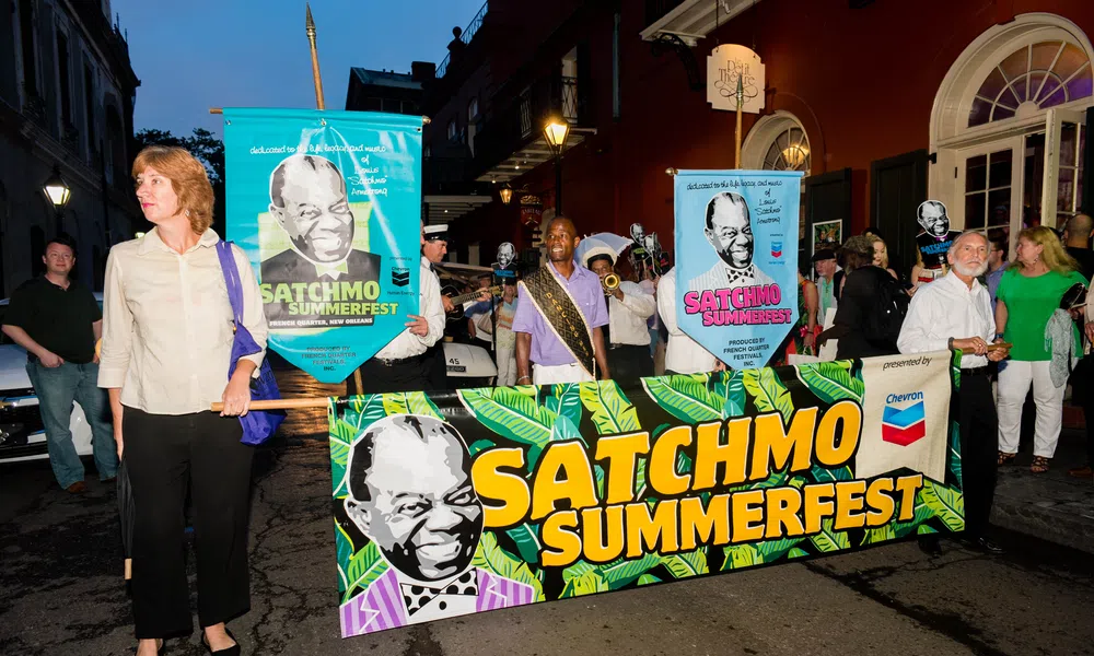 People holding colorful banners for Satchmo Summerfest during an evening street parade in New Orleans.