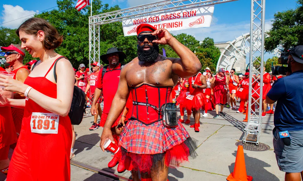 Crowd in red dresses at NOH3 Red Dress Run start/finish line on a sunny day with festive atmosphere.